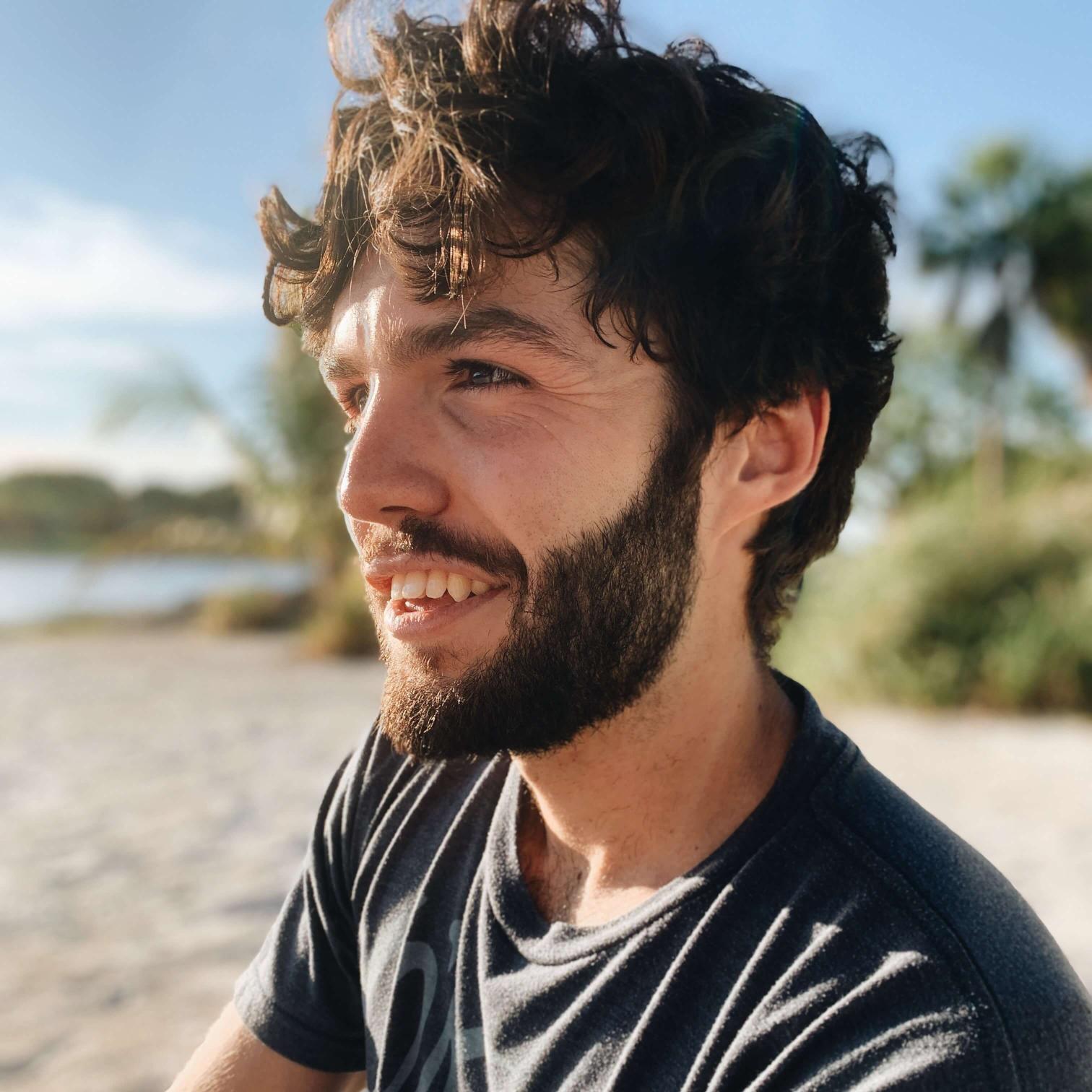 Man with short curly hair sitting at the beach